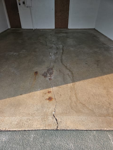 Bare uncoated concrete garage floor in Wayzata with a crack running front to back, widening at the apron, and rust and oil staining across the slab