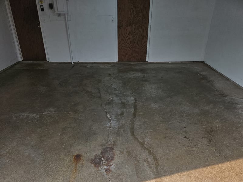 Bare uncoated concrete garage floor in Wayzata with a crack running front to back, widening at the apron, and rust and oil staining across the slab