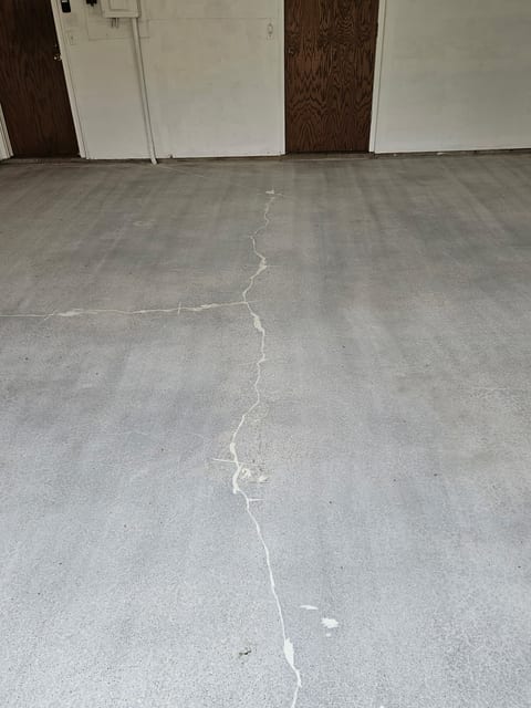 The same Wayzata garage floor diamond-ground to bare grey concrete, with the full-depth crack routed out and filled with white repair compound down the length of the slab