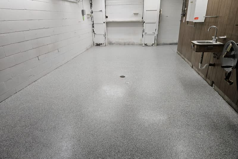 Coated basement utility room floor in polyurea with decorative flake, painted block walls, centre floor drain and a wall-mounted laundry sink